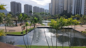 Zona ajardinada con fuente de agua, palmeras y vista a edificios altos al fondo.