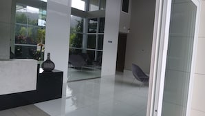Un área de recepción moderna con un separador de vidrio, un jarrón negro y una zona de estar con sillas.