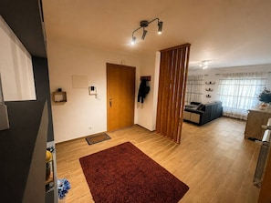 En moderne stue med en trædør, et rødt tæppe, en sofa og et køkkenområde med et køleskab.