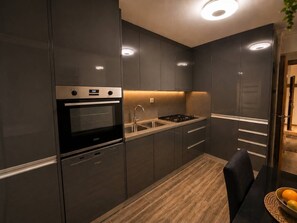 Una cucina moderna con mobili scuri, forno integrato, piano cottura a gas e lavello in acciaio inossidabile.
