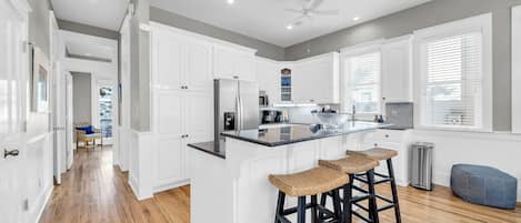 Una cocina moderna con armarios blancos, una isla central con taburetes de bar y un ventilador de techo.