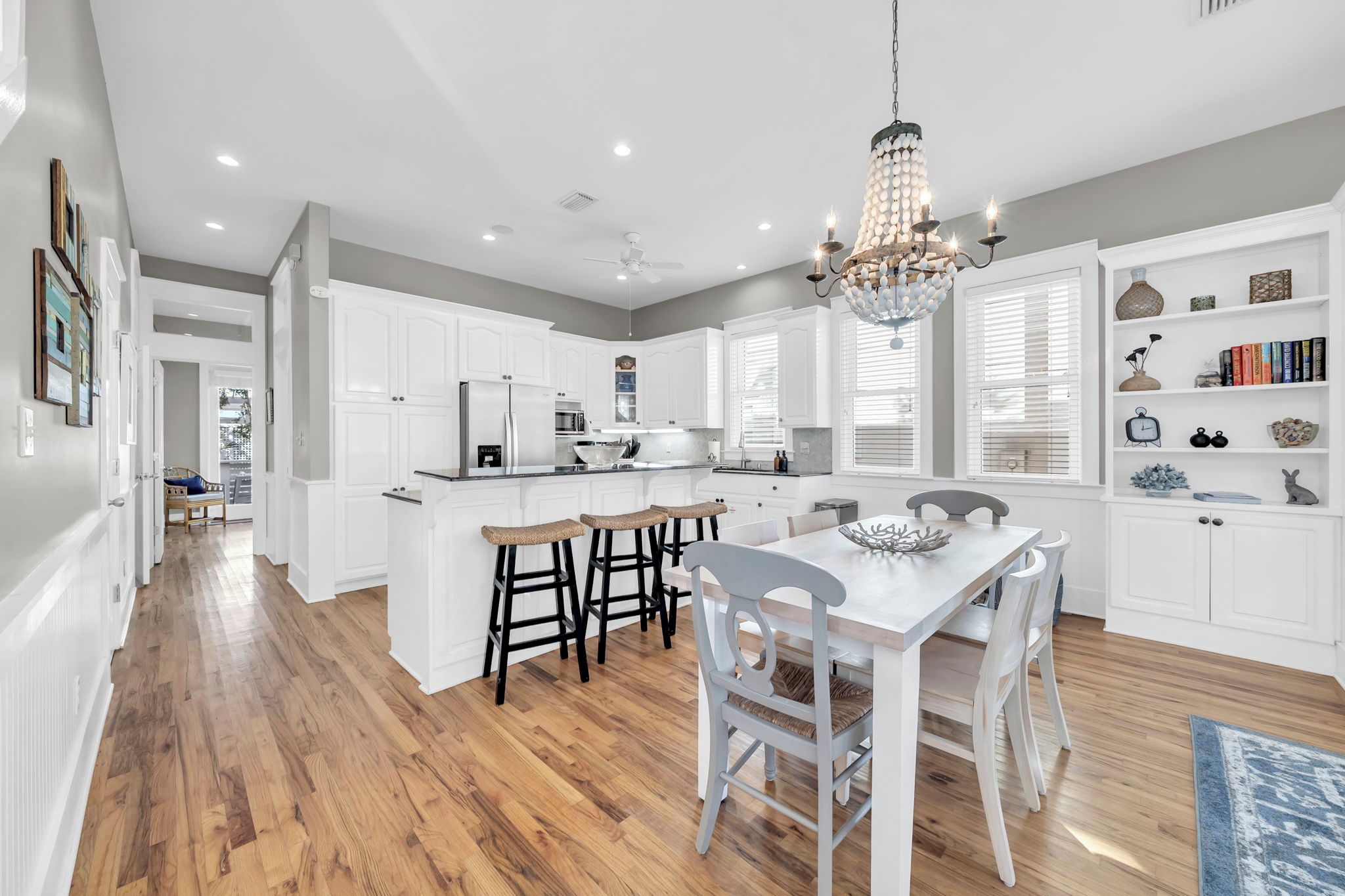 A modern kitchen with white cabinetry, a central island, and a dining area with a chandelier.