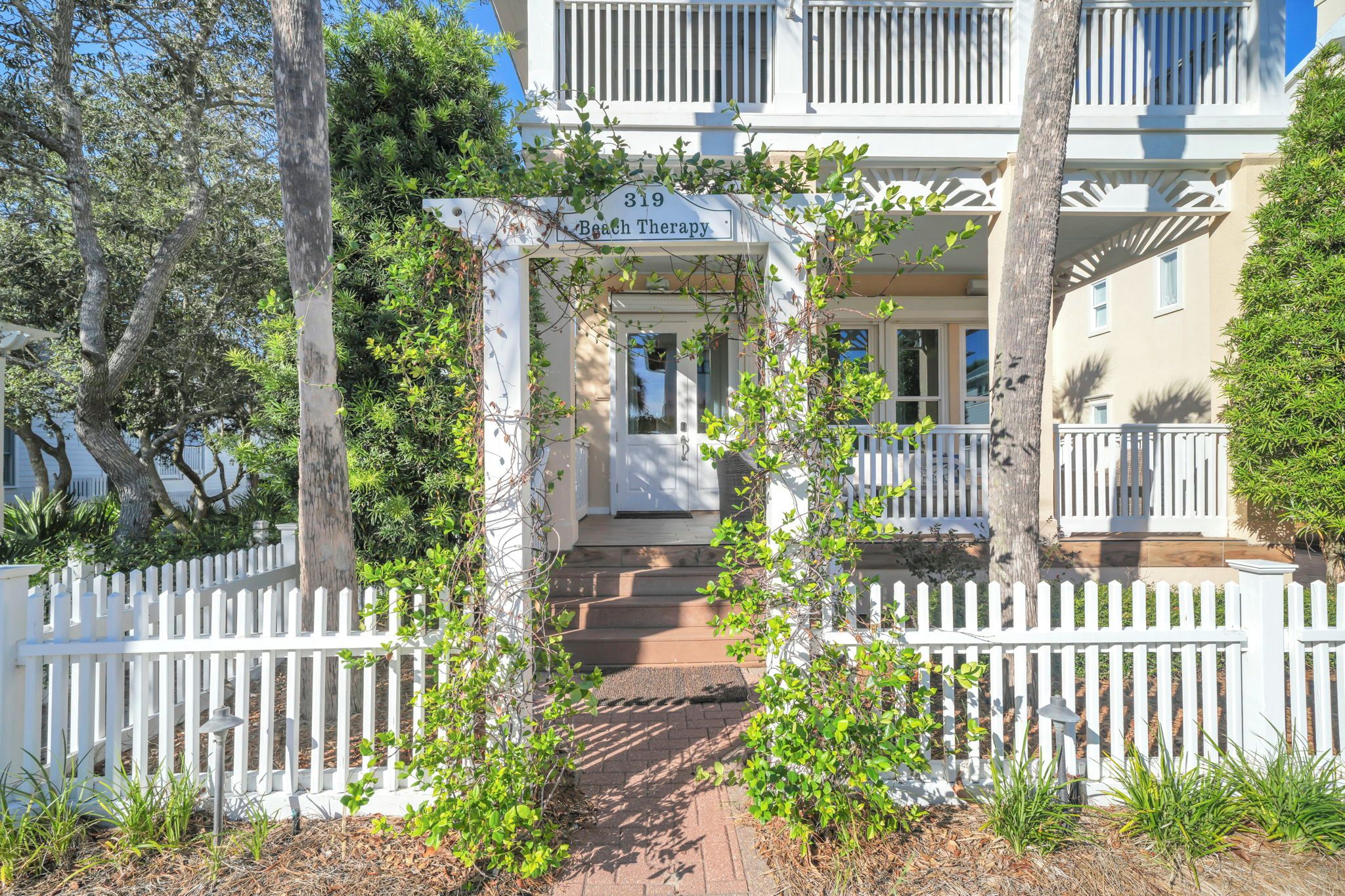 A building with a white facade, a porch with a white picket fence, and a sign reading '319 Beach Therapy'.