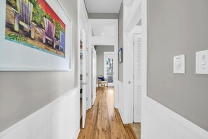 A hallway with white walls, wooden flooring, and a painting on the left. - When you need a getaway, Beach Therapy is the cure! (Panama City Beach)