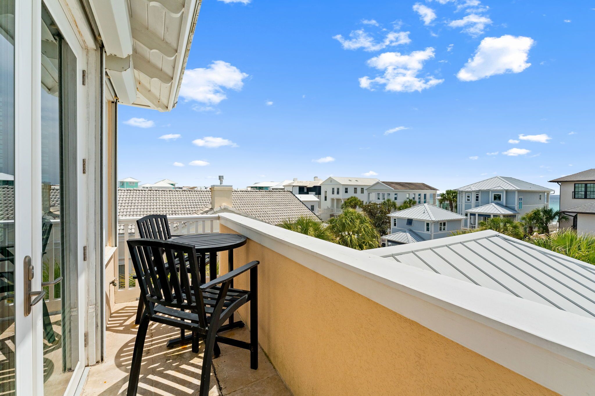 A balcony with a table and chairs, overlooking a residential area with houses and a clear sky.