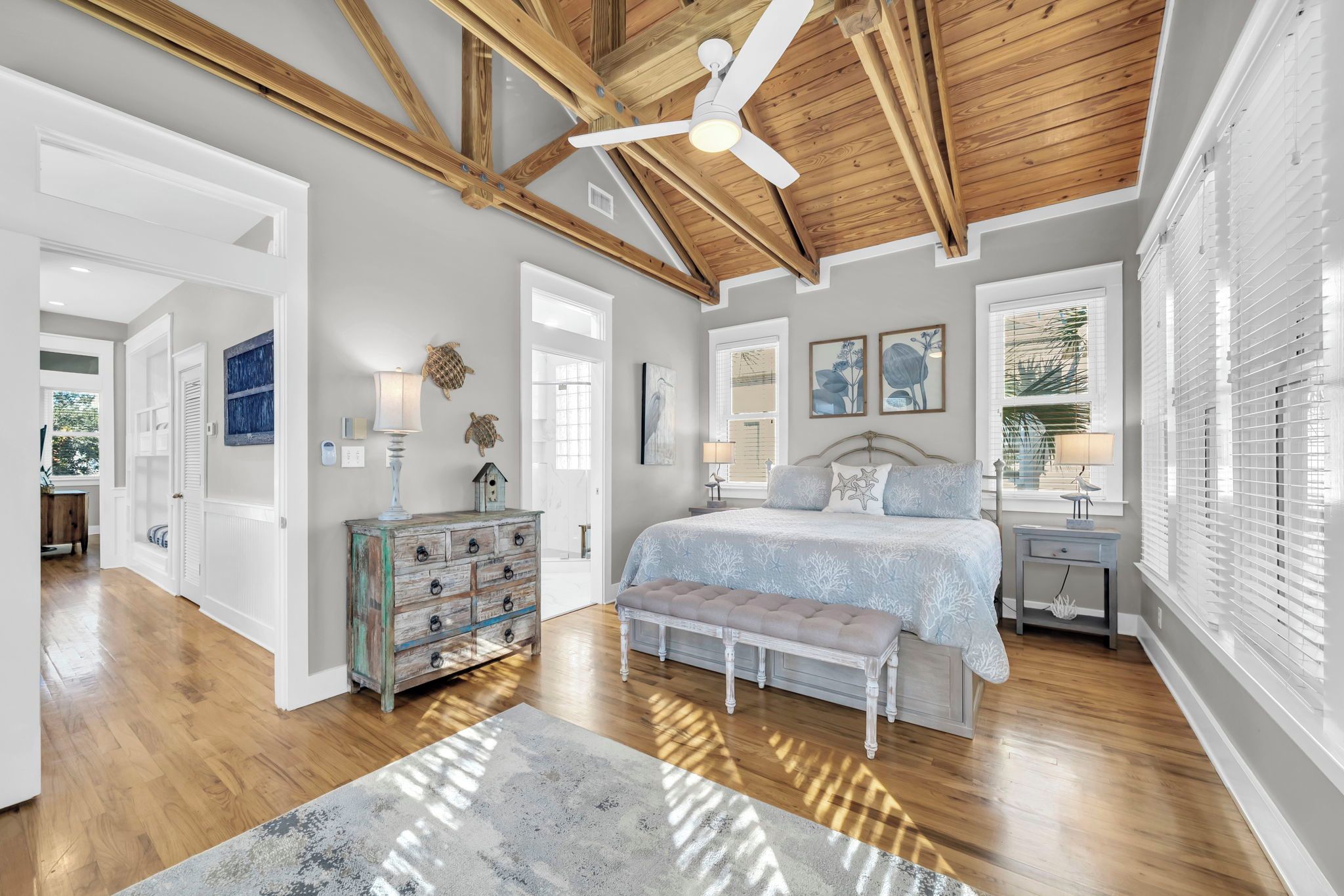 A bedroom with a wooden ceiling, a bed with a white bedspread, a bench, a dresser, and artwork on the walls.