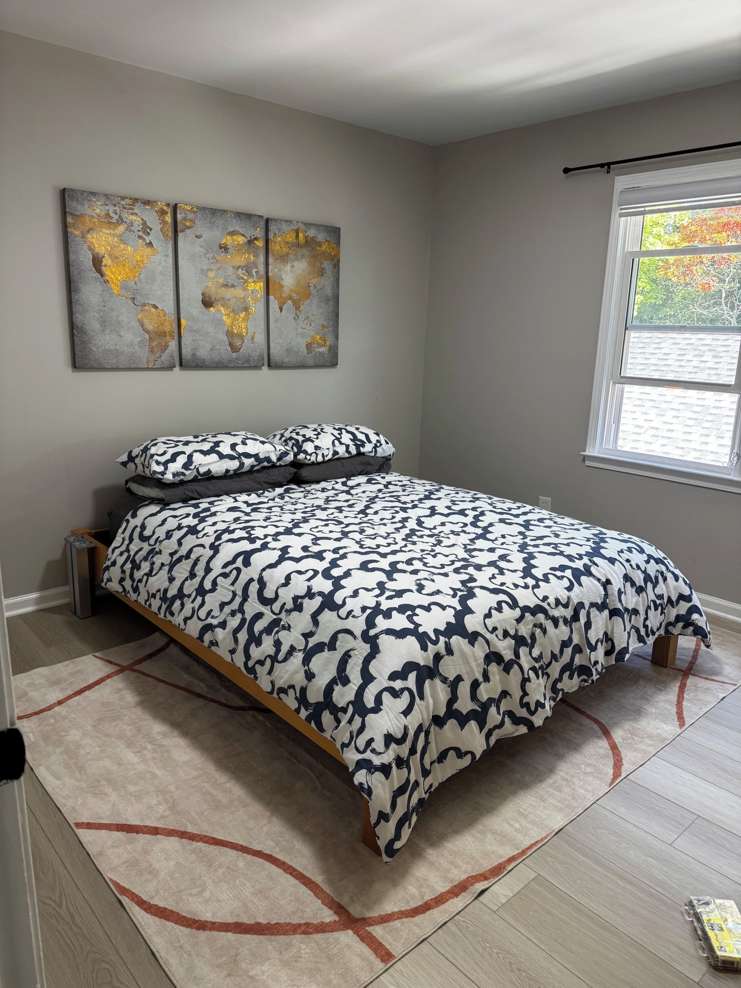 A bedroom with a bed, a world map artwork, a window, and a rug.