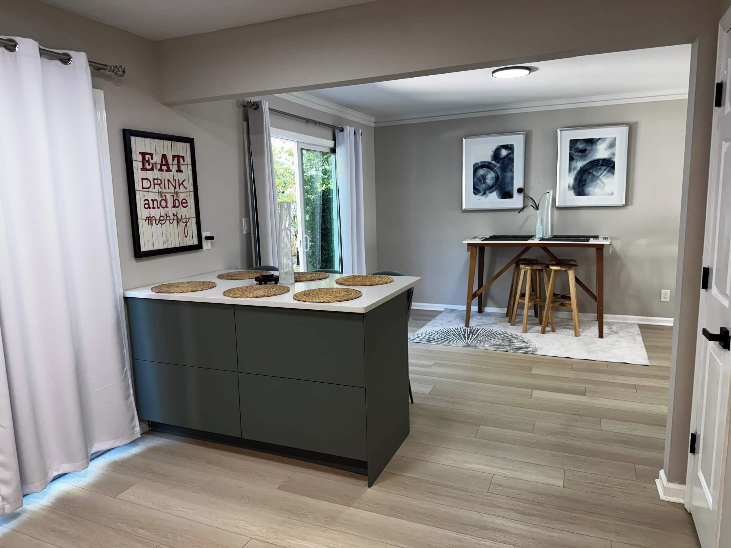 A modern kitchen with a central island, a dining area with a table and chairs, and artwork on the walls.