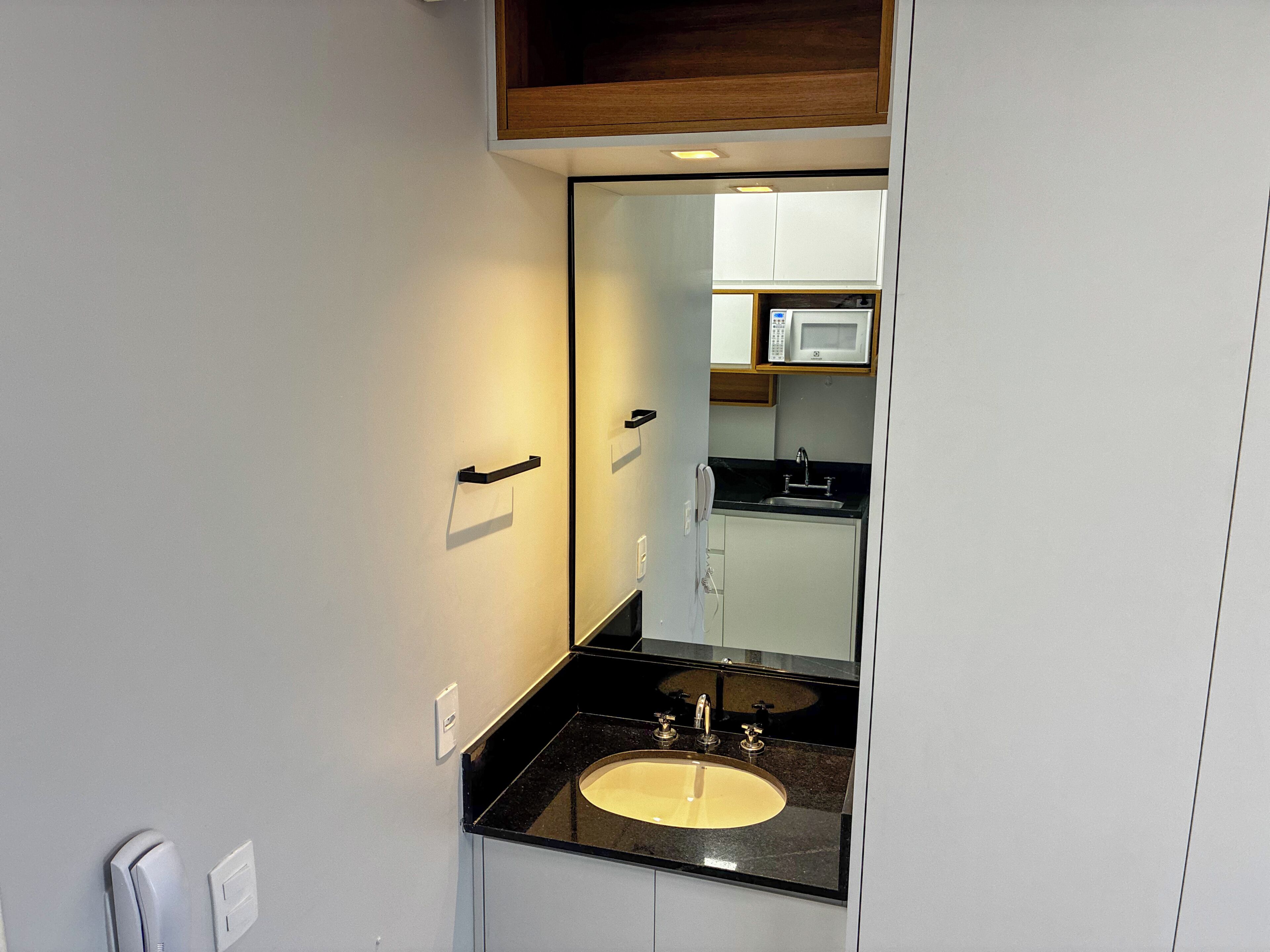 Un bagno con lavandino, specchio e un forno a microonde sullo sfondo.