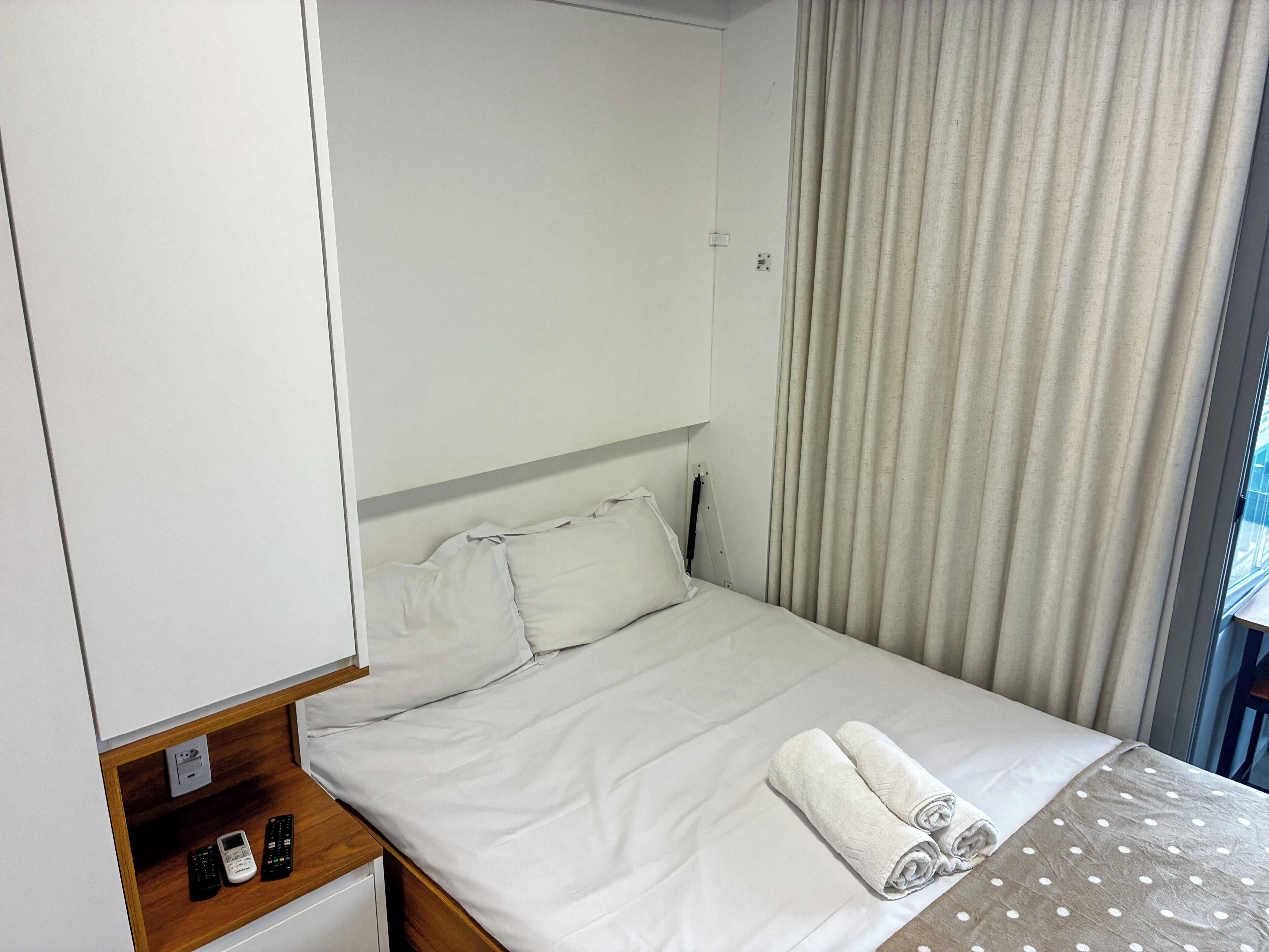 Een hotelkamer met een bed, nachtkastje, telefoon en een raam met gordijnen.
