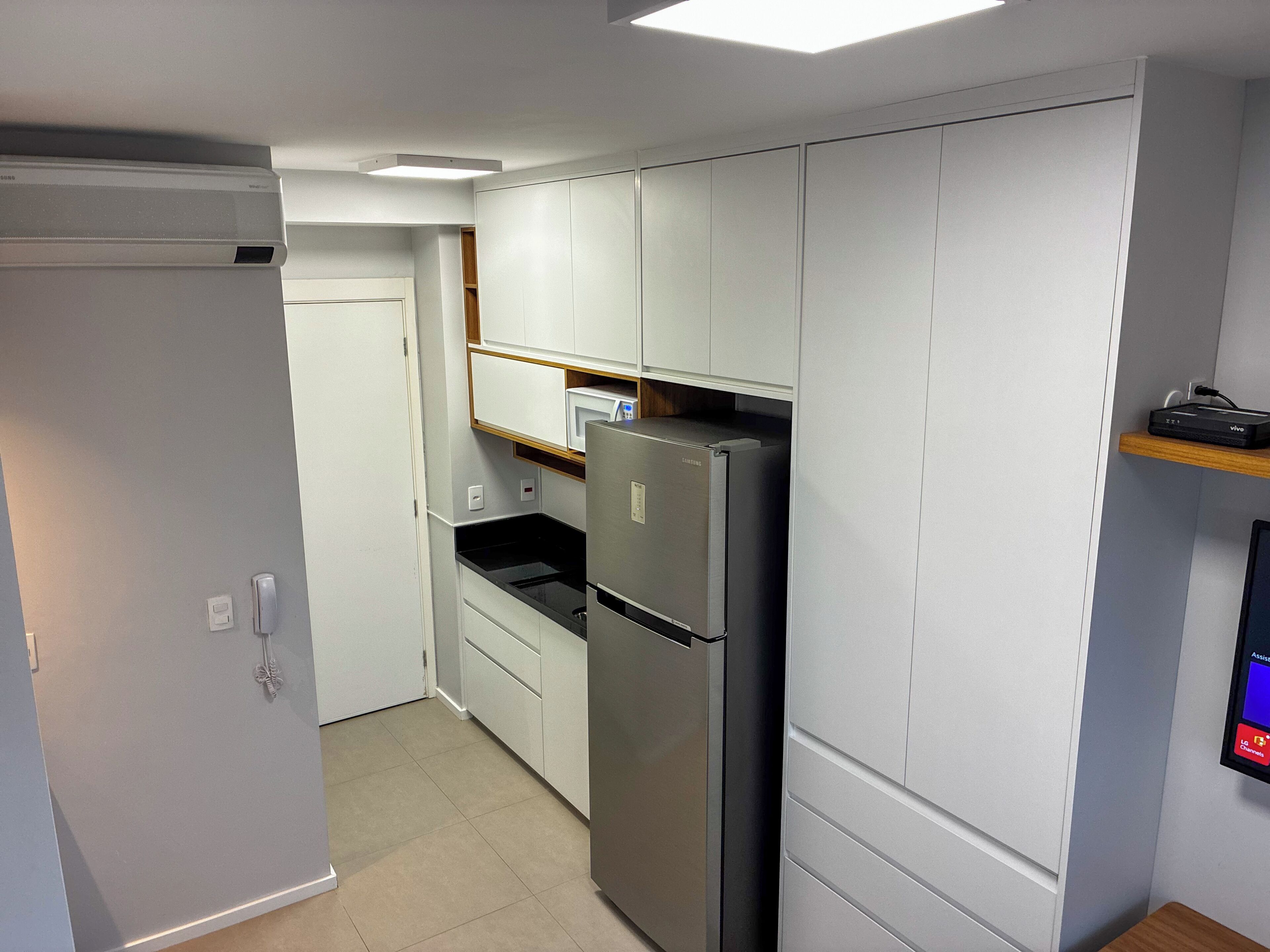Eine kompakte Küche mit weißen Schränken, einer eingebauten Mikrowelle und einem Edelstahl-Kühlschrank.