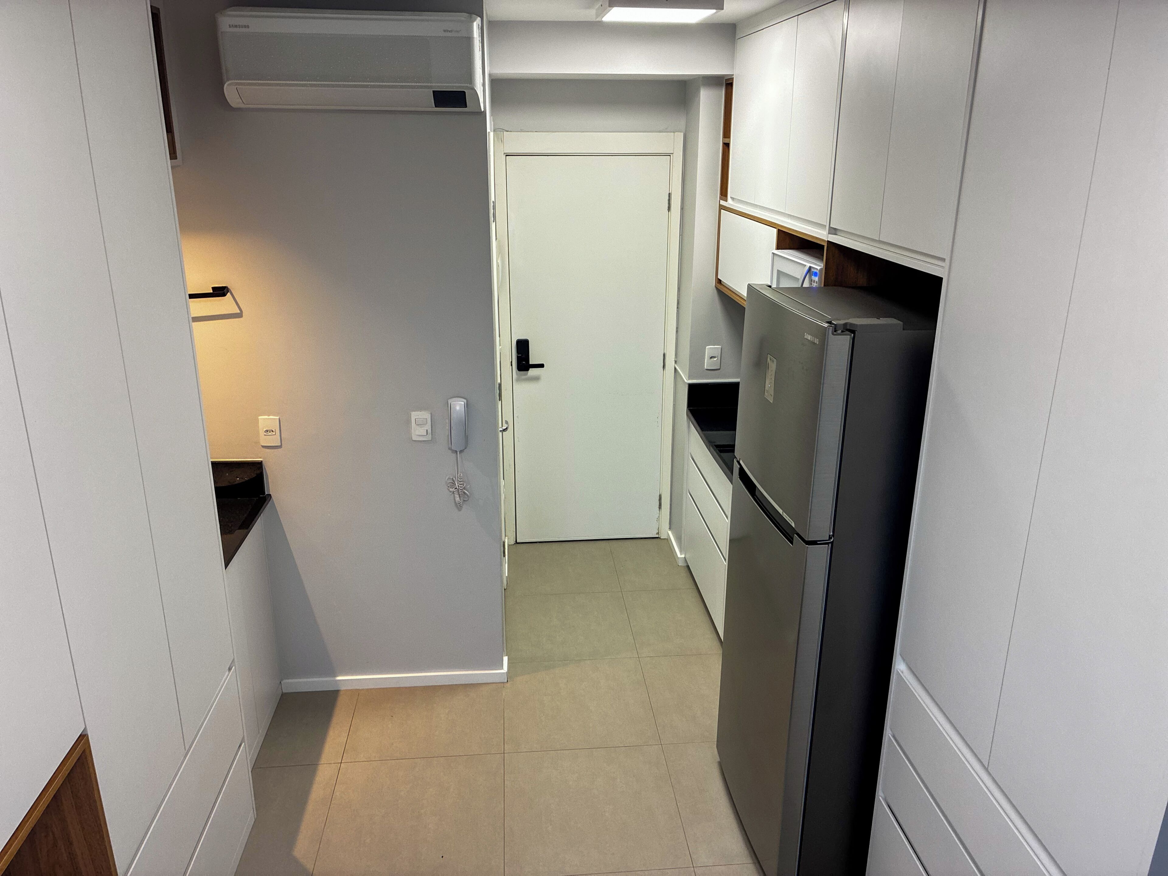 Una cucina compatta con mobili bianchi, un frigorifero integrato, un forno a microonde e un piccolo piano di lavoro.