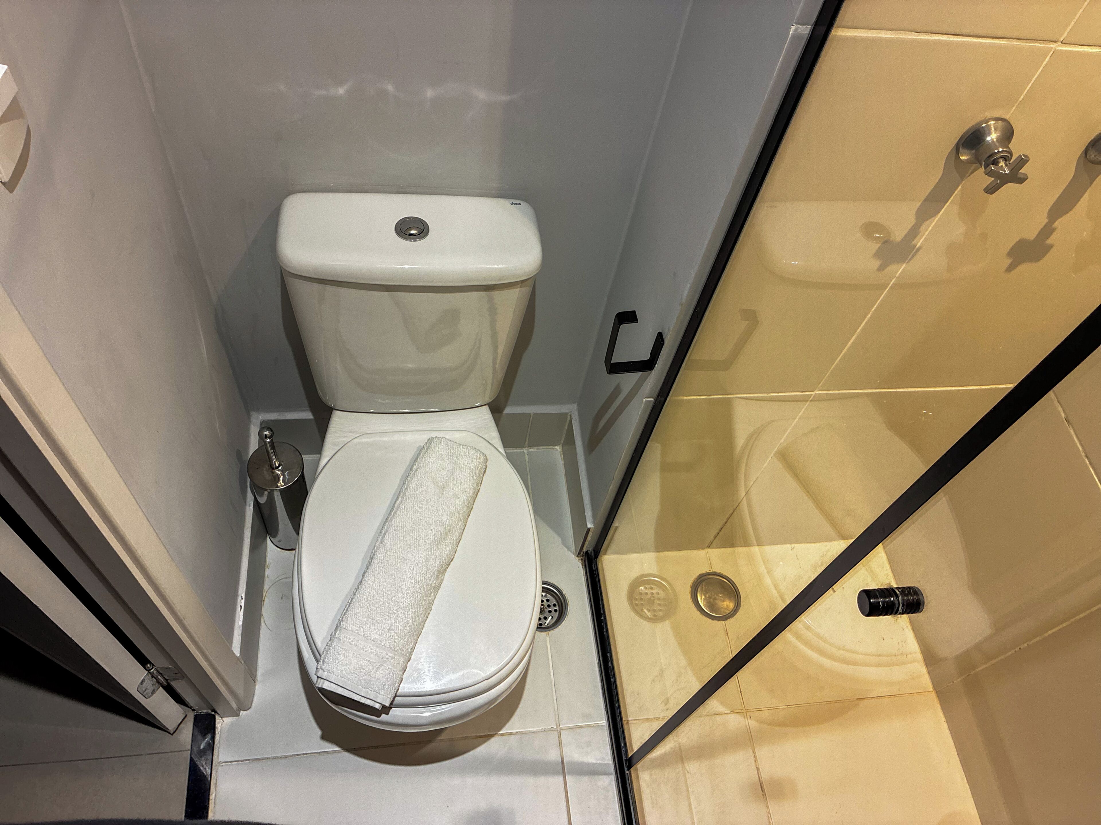 A toilet with a towel on the seat, a shower area with a glass door, and a visible drain.