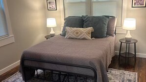 Ein Schlafzimmer mit einem Bett, zwei Nachttischlampen, einem Deckenventilator und einem Fenster mit Jalousien.