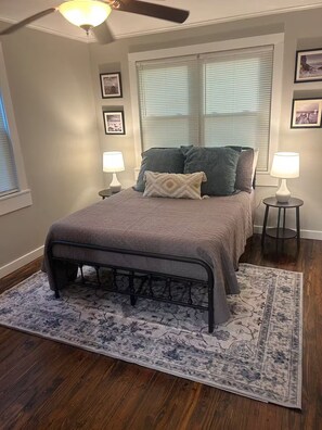 A bedroom with a bed, two bedside lamps, a ceiling fan, and a window with blinds. - Pixie’s Haven A Home Away From Home (Monroe)