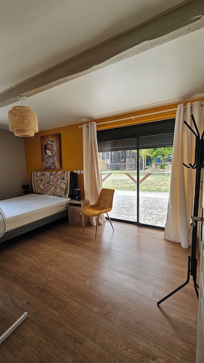 Een kamer met een bed, een stoel, een tafel, een lamp en een schilderij aan de muur.