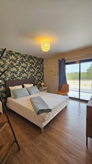 Een slaapkamer met een bed, nachtkastje, stoel, raam met uitzicht en een plafondlamp.