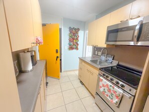 A compact kitchen with a microwave, stove, sink, and a yellow door. - Surfer's Sanctuary at Waikiki Beach (Honolulu)