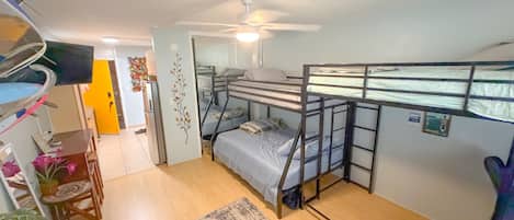 A compact room with bunk beds, a ceiling fan, a small table with a chair, and a rug on the floor.