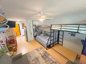 A compact room with bunk beds, a ceiling fan, a small table with a chair, and a rug on the floor. - Surfer's Sanctuary at Waikiki Beach (Honolulu)