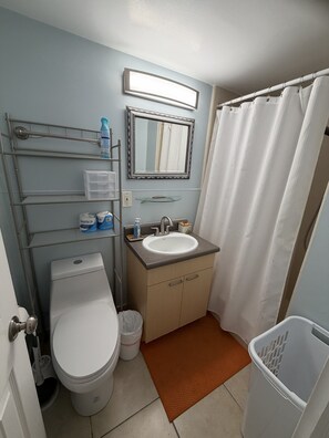 A bathroom with a toilet, sink, mirror, and shower curtain. - Surfer's Sanctuary at Waikiki Beach (Honolulu)