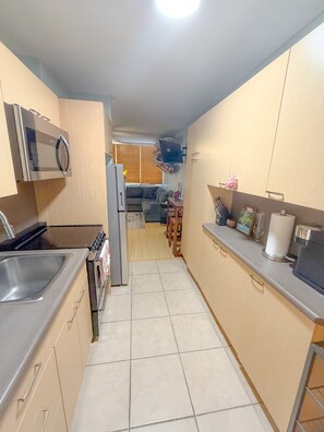 A kitchen with a microwave, stove, and sink. There is a dining area with a sofa and table in the background. - Surfer's Sanctuary at Waikiki Beach (Honolulu)