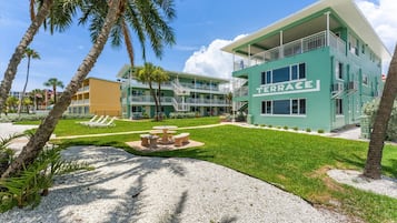 A multi-story hotel with a green facade, a pool area with lounge chairs, and a clear sky.