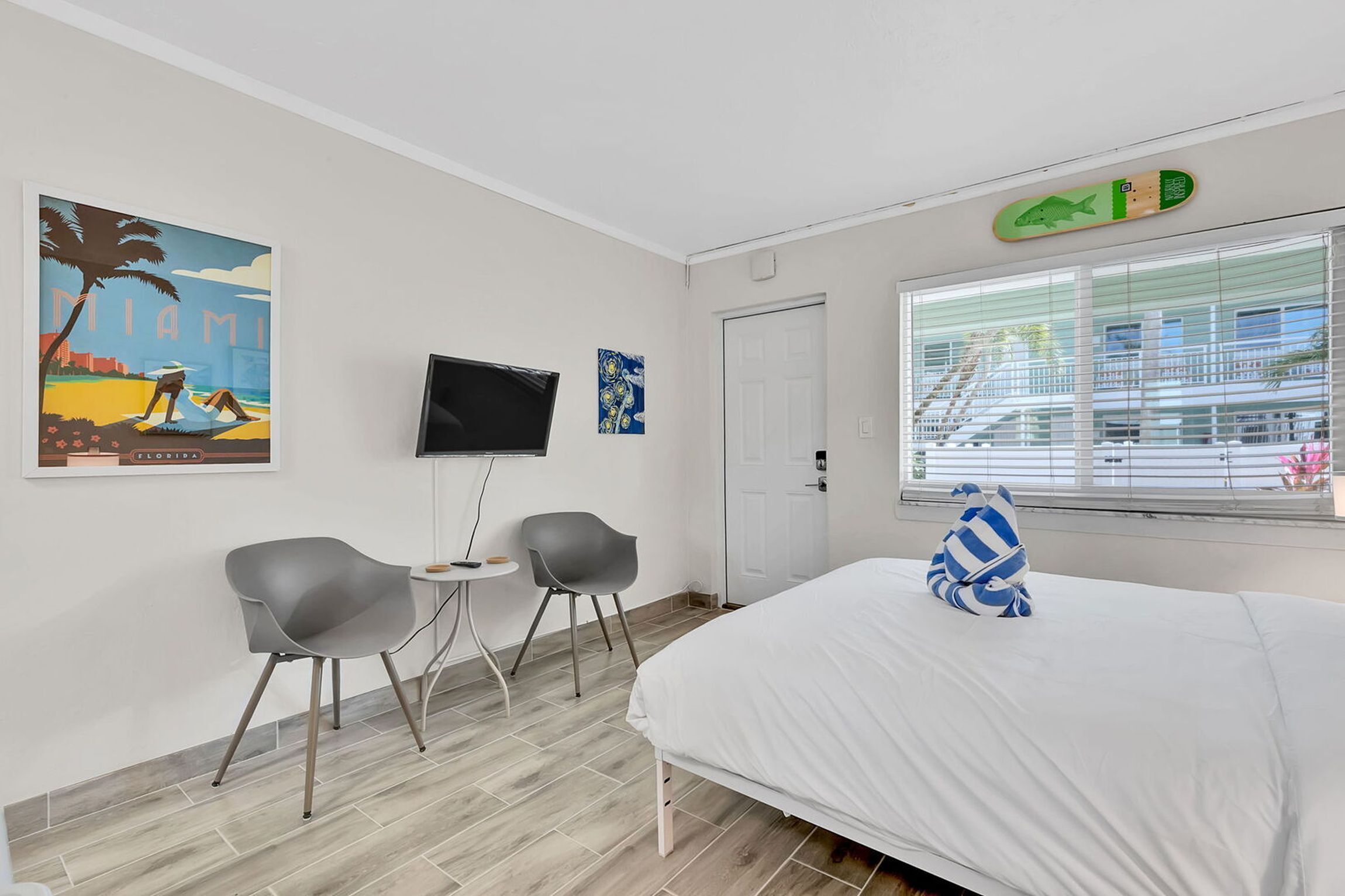 A hotel room with a bed, two chairs, a TV, and artwork on the walls.