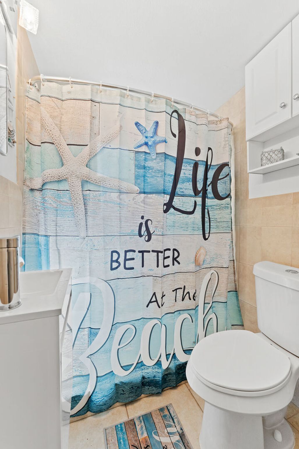 Ein Badezimmer mit einer Duschvorhangs, der ein Strandmotiv und den Schriftzug 'Life is better at the beach' zeigt.