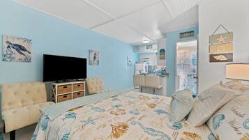 A bedroom with a bed, a television, a dresser, and a dining area.