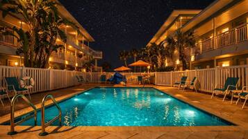 A swimming pool with a starry night sky above, surrounded by palm trees and lounge chairs.