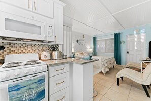 Una cocina compacta con armarios blancos, un horno y un microondas. Hay un pequeño comedor con una mesa y una silla.