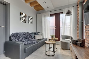 A modern living room with a grey sofa, a round wooden table, a grey armchair, and a brick accent wall. - Waterlane Island - Pool Sauna and Gym (Gdańsk)