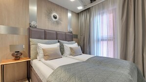 Ein modernes Schlafzimmer mit einem großen Bett, einem Nachttisch, einem wandmontierten Spiegel und einem Fenster mit Vorhängen.