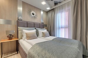 A modern bedroom with a large bed, a nightstand, a wall-mounted mirror, and a window with curtains. - Waterlane Island - Pool Sauna and Gym (Gdańsk)