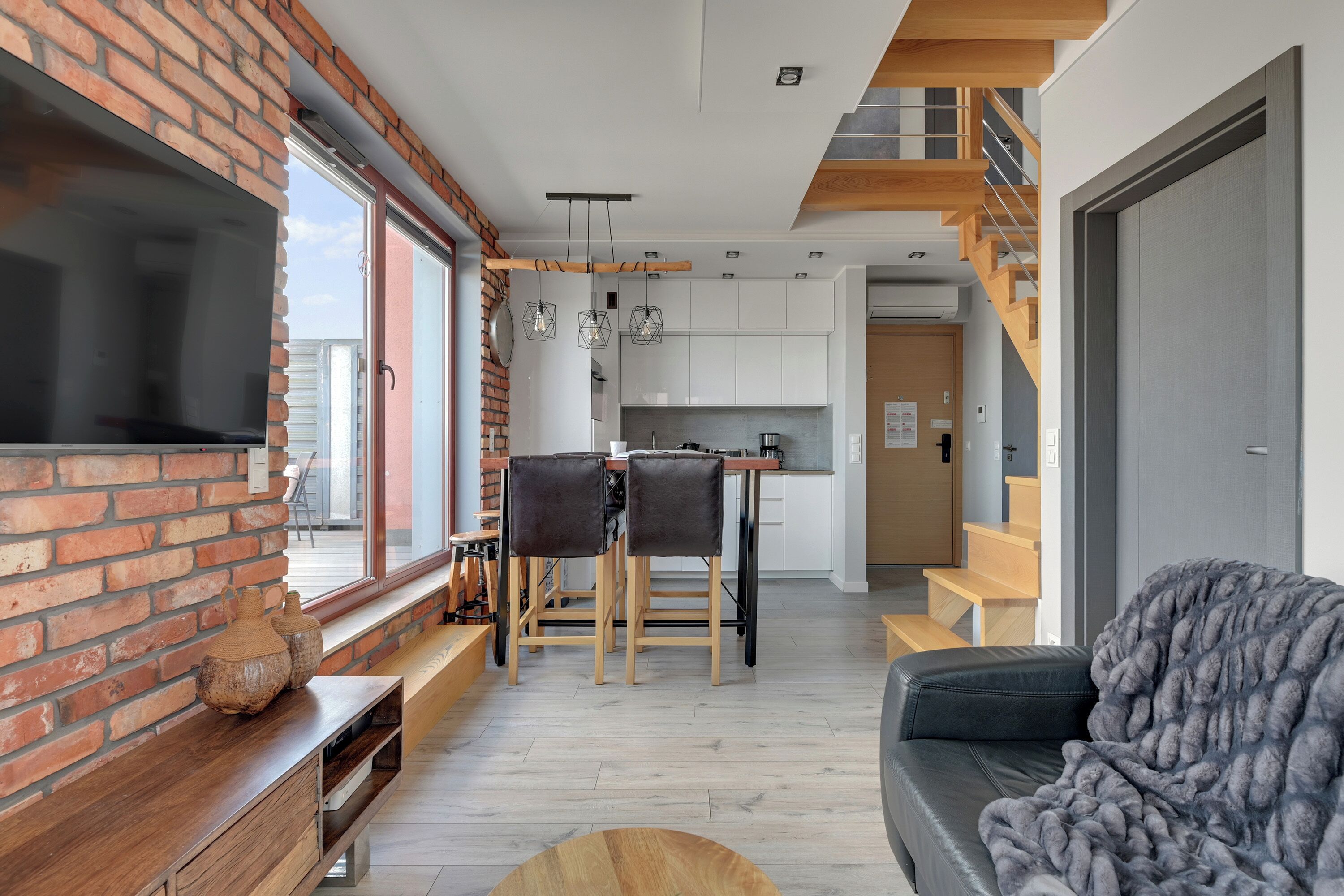 En moderne stue med en murstensvæg, en sofa, et fjernsyn og et spiseområde med et bord og stole.