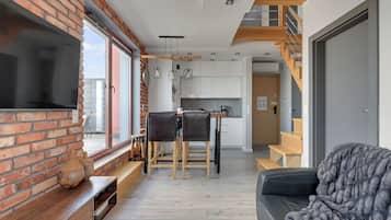 En moderne stue med en murstensvæg, en sofa, et fjernsyn og et spiseområde med et bord og stole.