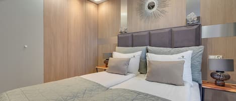 A modern bedroom with a large bed, a headboard with built-in lighting, a decorative wall piece, and a bedside table with a lamp.