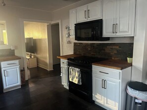 A modern kitchen with white cabinetry, a black stove, and a microwave. - Relaxing Coastal Getaway – Near Beach & Shops (Clearwater)