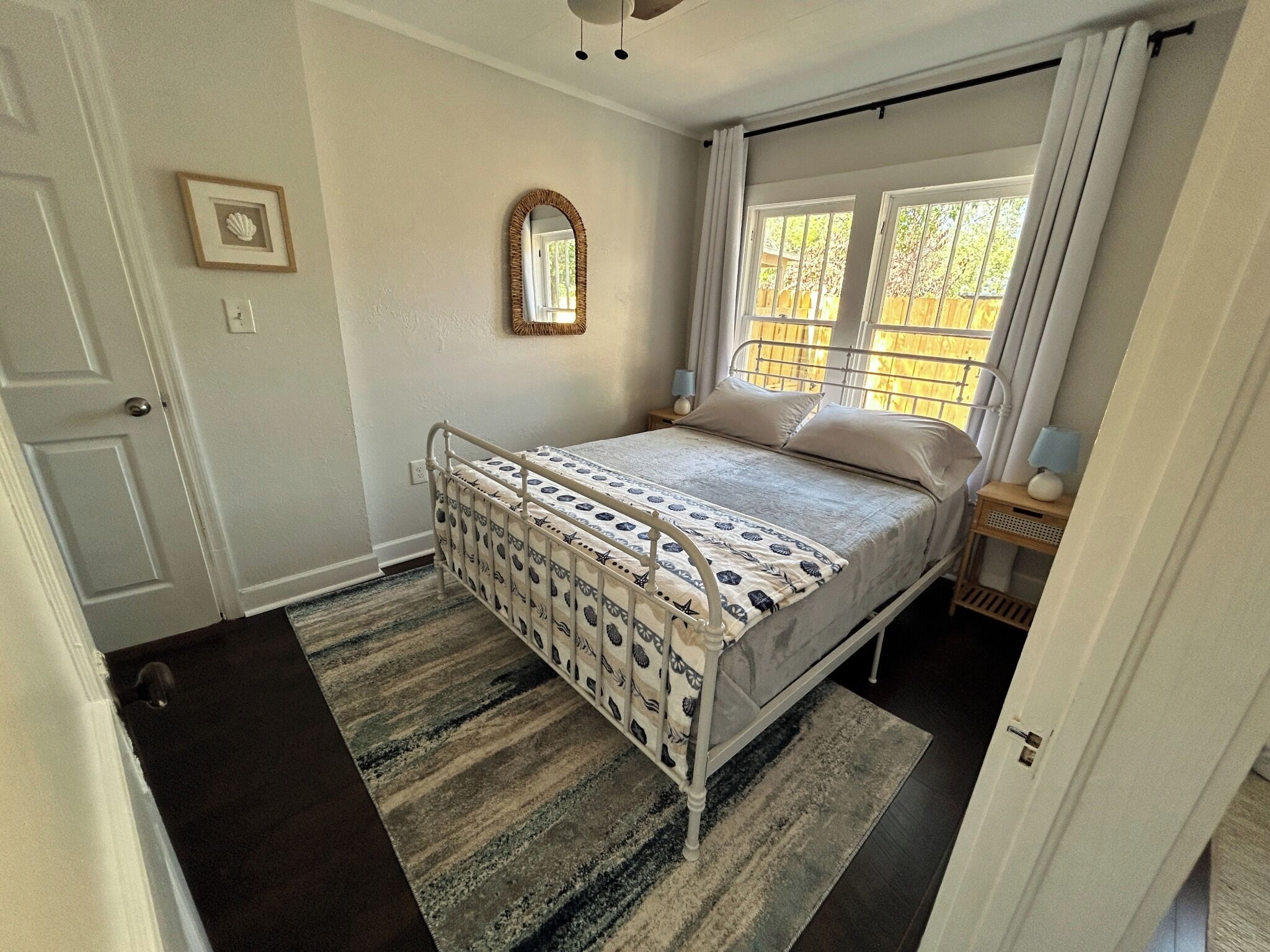 A bedroom with a bed, a window, a door, and a small bedside table.