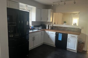 A kitchen with white cabinets, a black refrigerator, a wooden countertop, and a window with curtains. - Relaxing Coastal Getaway – Near Beach & Shops (Clearwater)
