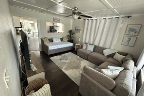 A living room with a sofa, a bed, a ceiling fan, and a television. - Relaxing Coastal Getaway – Near Beach & Shops (Clearwater)