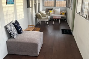 En smal korridor med en grå soffa, flätade stolar och en bänk med kuddar.