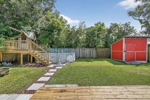A backyard with a wooden deck, a red shed, and a wooden playhouse with a staircase. - Relaxing Coastal Getaway – Near Beach & Shops (Clearwater)