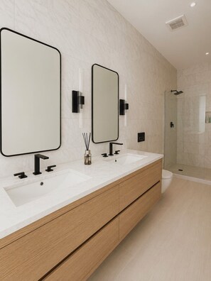 Une salle de bain moderne avec deux lavabos, un grand miroir et une douche à parois de verre.