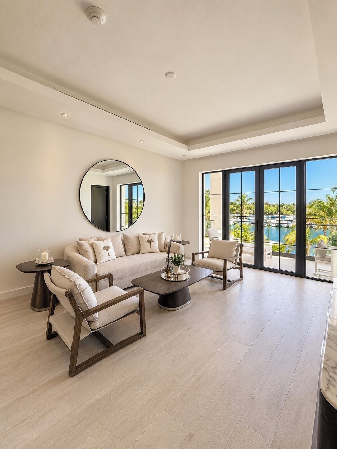 A spacious living room with a large window, a round mirror, and a modern sofa set.