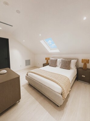 Ein Schlafzimmer mit Dachfenster, einem Bett mit Kissen, einem Nachttisch und einem Beistelltisch.