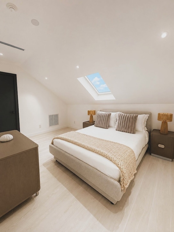 Une chambre avec un puits de lumière, un lit avec des oreillers, une table de chevet et une commode.