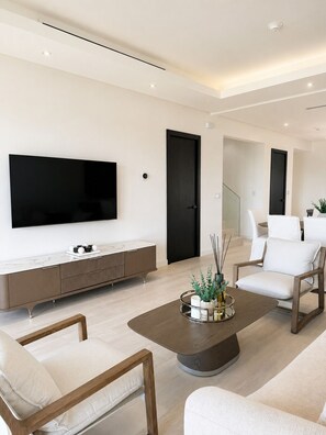 Ein modernes Wohnzimmer mit einem Flachbildfernseher, einem Holztisch und weißen Möbeln.