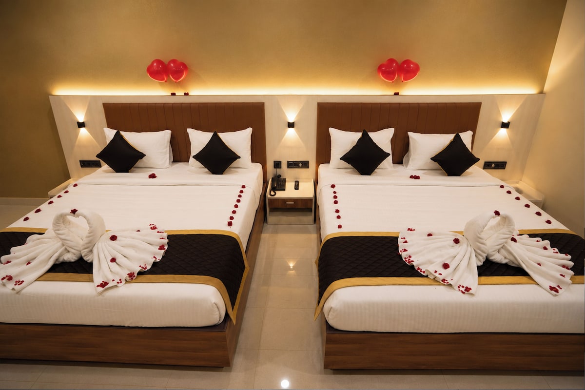 Two identical twin beds with a wooden headboard, white bedding, black pillows, and a decorative towel with red flowers.